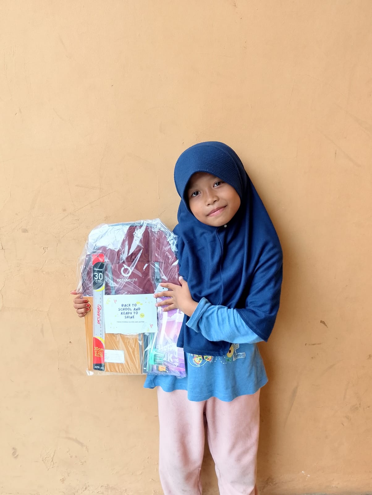 A student in Indonesia holding a wrapped back-to-school supply kit with a ruler and notebooks.