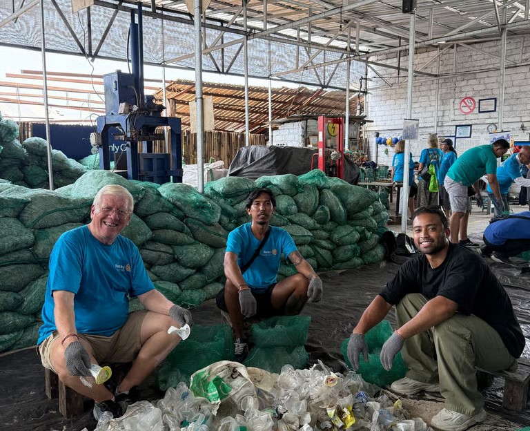 Jimmy Thomas kneeling with other volunteers sorting recyclables at an environmental service initiative in Indonesia.